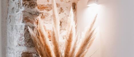 Un intérieur rustique avec un mur en pierre, une poutre en bois et un vase contenant des plumes d’herbe de la pampa.
