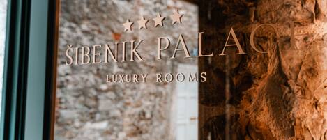 A sign for "Sibenik Palace Luxury Rooms" with a stone wall background.