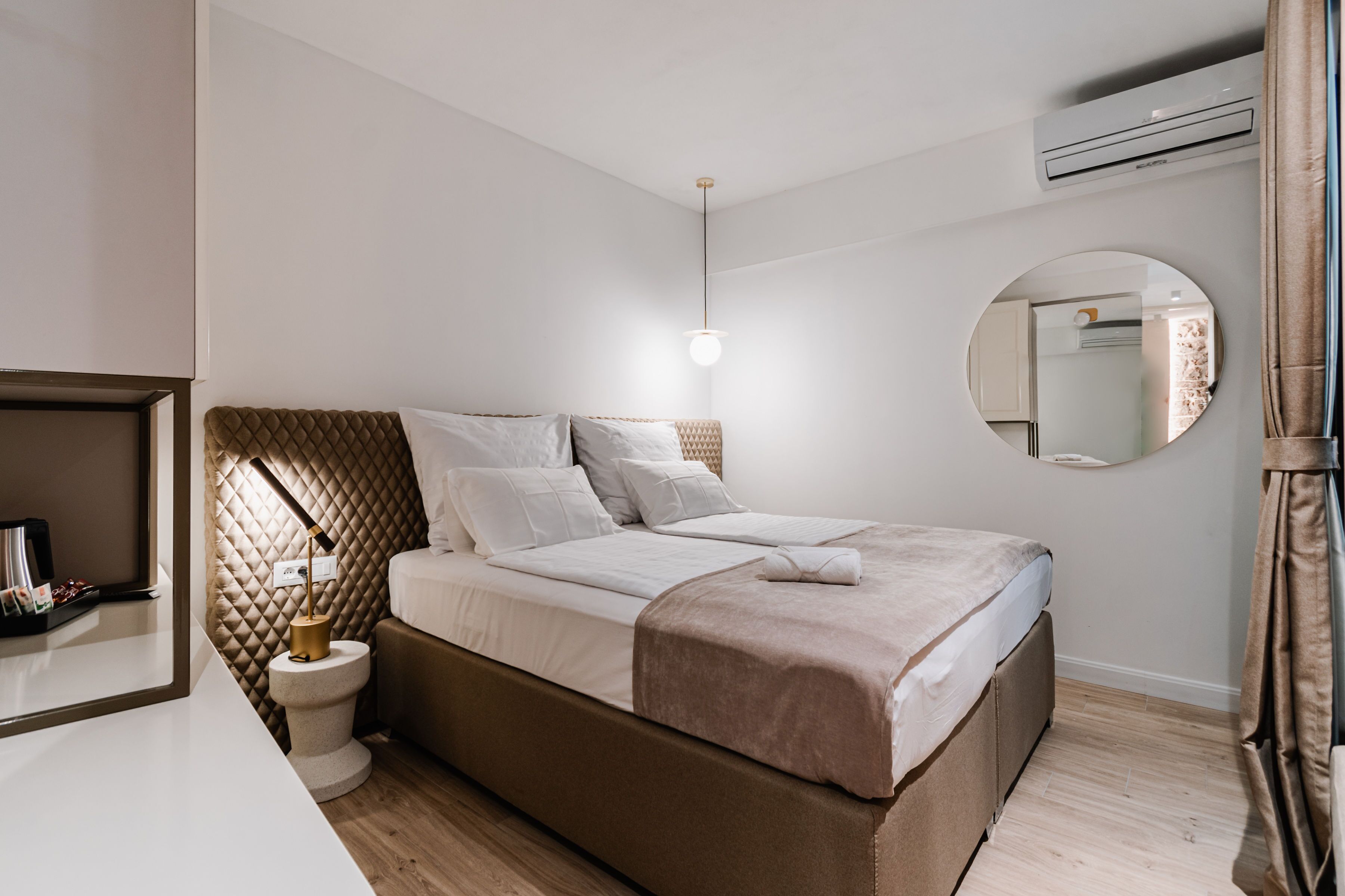 Un dormitorio moderno con cama, mesita de noche, lámpara y un espejo redondo en la pared.