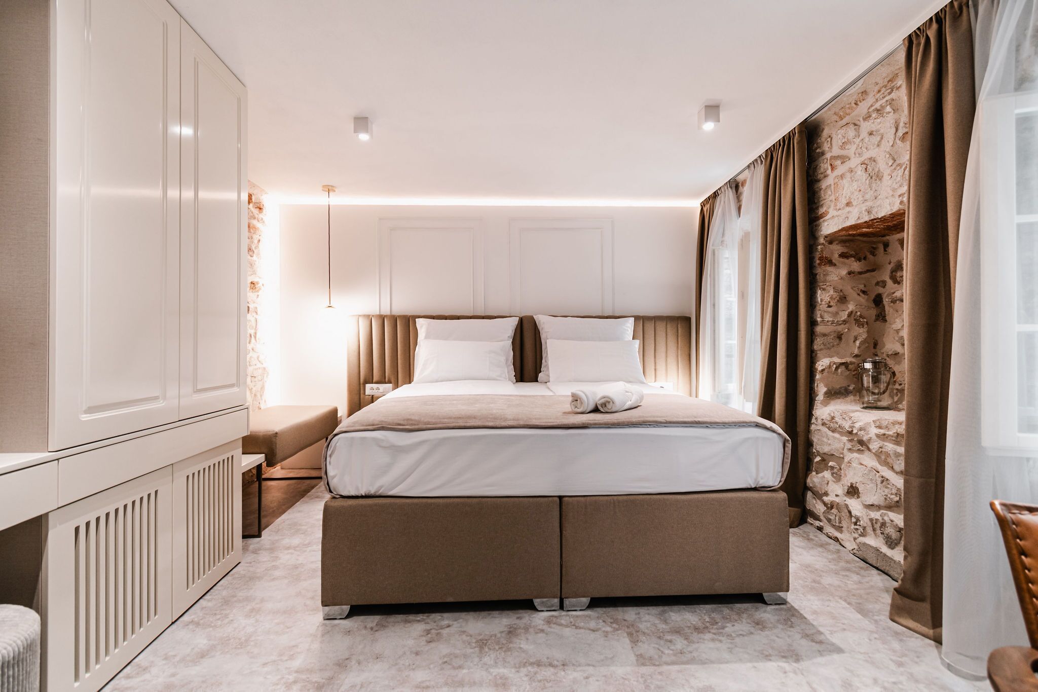 Een moderne slaapkamer met een groot bed, een inbouwkast, een accentmuur van steen en een knus zithoekje.