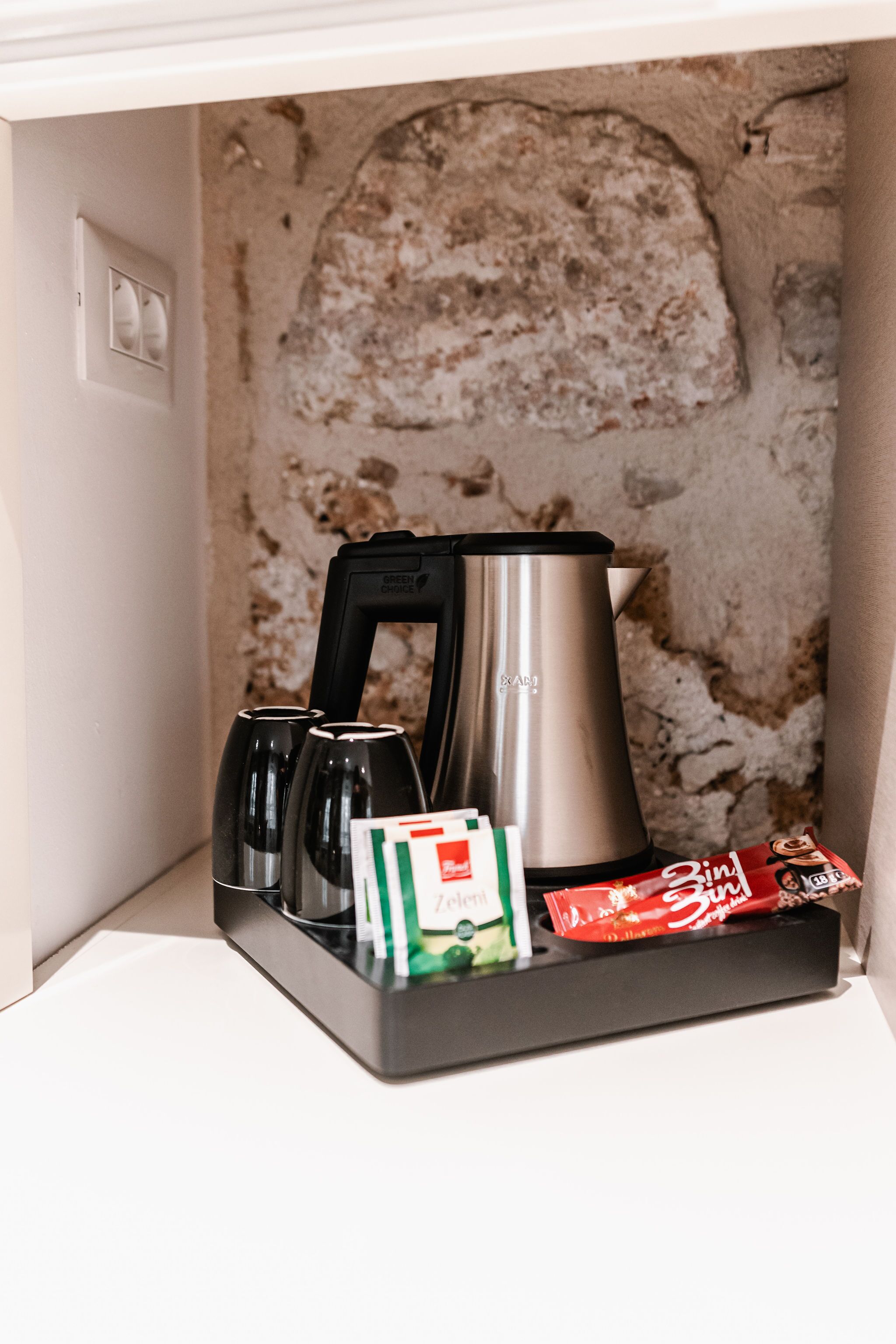 A coffee maker, tea kettle, and tea bags on a tray in a kitchen area with a textured wall.