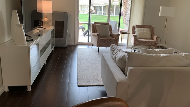 Un soggiorno moderno con televisione a schermo piatto, un divano, due poltrone, un tavolino da caffè e una porta scorrevole in vetro che dà su un patio esterno.