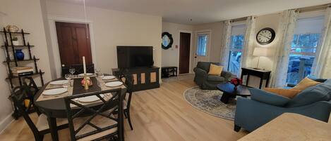 A living room with a TV, a dining table set for four, a sofa, and a chair.