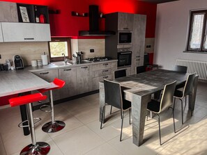A modern kitchen with a dining area, featuring a large island, red bar stools, and a dining table with chairs.