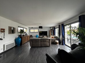 A modern living room with a grey sofa, a TV, and a large window with curtains.
