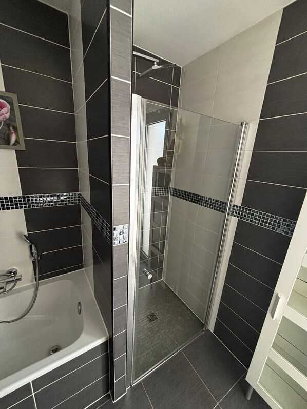 A modern bathroom with a shower, a bathtub, and tiled walls.