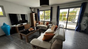 Un salon moderne avec un canapé, une table basse, un téléviseur et une grande fenêtre avec des rideaux.