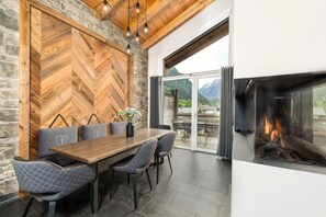 A dining area with a wooden herringbone wall, a fireplace, and a view of mountains.