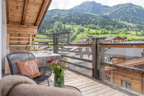 Ein Holzbalkon mit Blick auf eine Berglandschaft, ein Sessel mit Kissen und eine Vase mit Blumen.