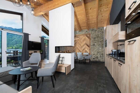 A modern kitchen with wooden cabinets, a stone wall, and a dining area with grey chairs.