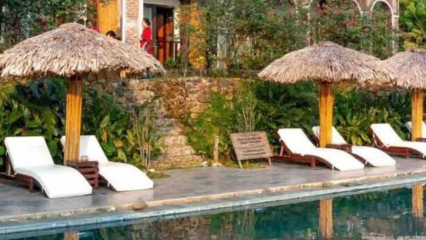 A poolside area with lounge chairs and thatched umbrellas, surrounded by lush greenery. - 2 BR con patio por el centro comercial (Bloomington)