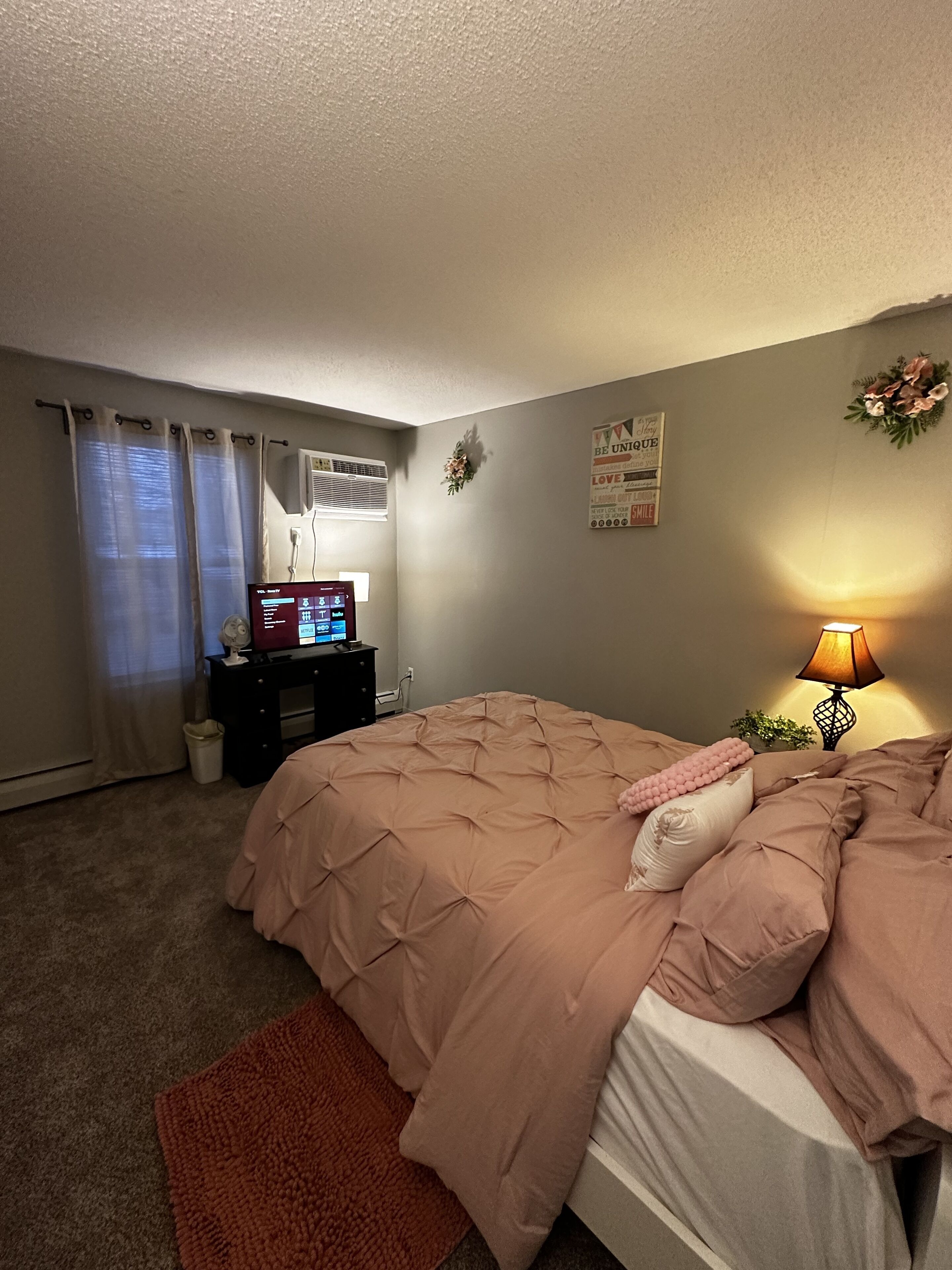 A bedroom with a bed, a desk, a lamp, and a wall decoration.