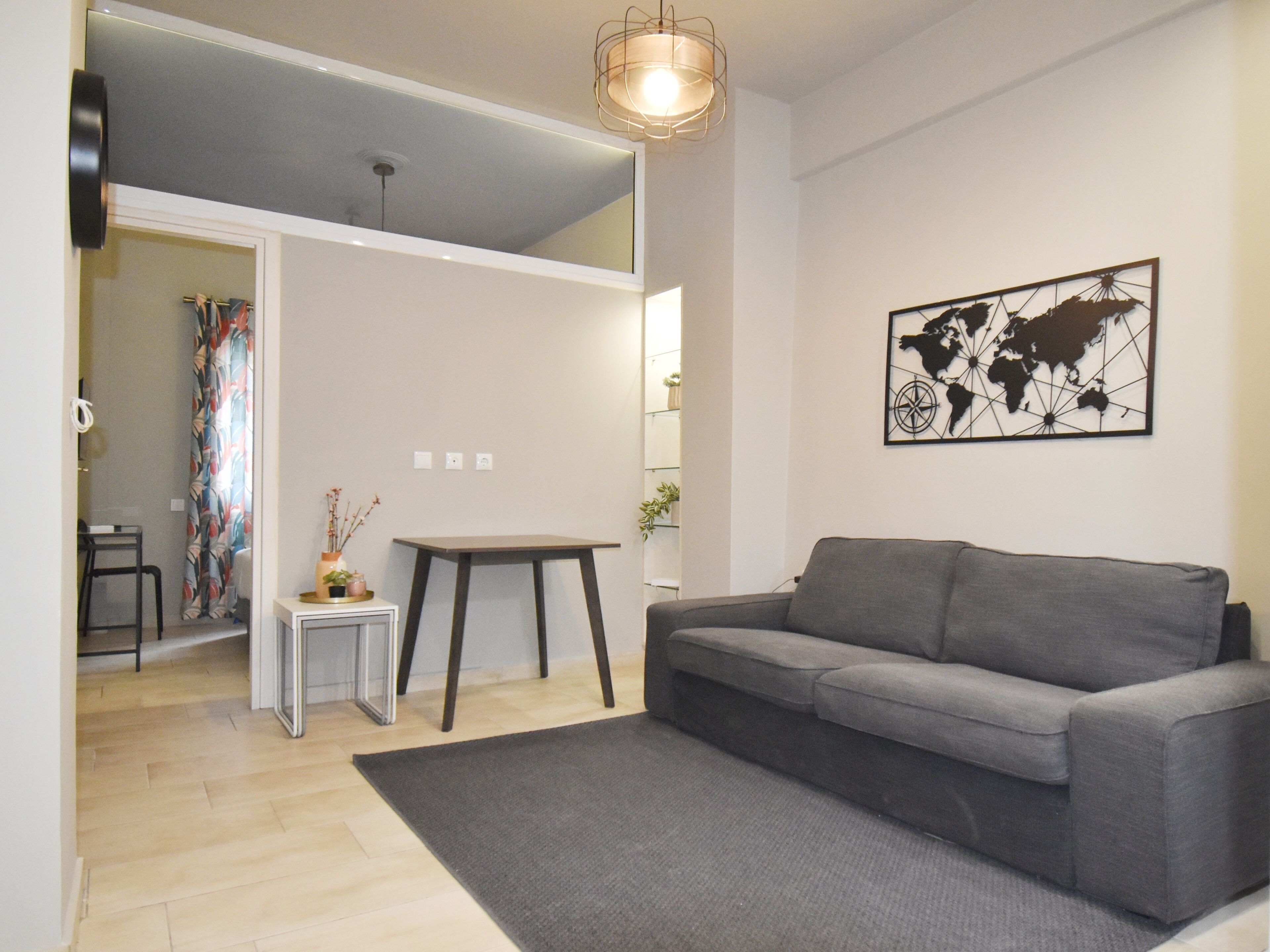 A modern living room with a grey sofa, a small side table, a world map artwork, and a wooden floor.