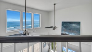 A room with three large windows offering ocean views, a ceiling fan, and a painting on the wall. - Perfect, beachfront pet friendly 5 bedroom home, close to waters (Gulf Shores)