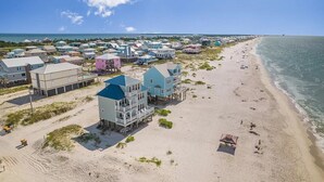 A beachfront property with multiple houses, some elevated on stilts, and a sandy beach. - Perfect, beachfront pet friendly 5 bedroom home, close to waters (Gulf Shores)