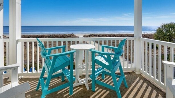 A covered outdoor area with a view of the beach, featuring two turquoise chairs and a small table. - Beachfront Bliss Ocean Pier 4 Oceanfront 2 bed 2 bath Windy Hill (North Myrtle Beach)