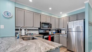 A modern kitchen with grey cabinets, stainless steel appliances, a marble countertop, and a clock on the wall. - Beachfront Bliss Ocean Pier 4 Oceanfront 2 bed 2 bath Windy Hill (North Myrtle Beach)