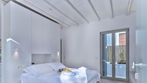 A modern bedroom with a bed, bedside table, and a sliding glass door leading to an outdoor area. - Fully equiped, spacious cozy apartment (Paros)