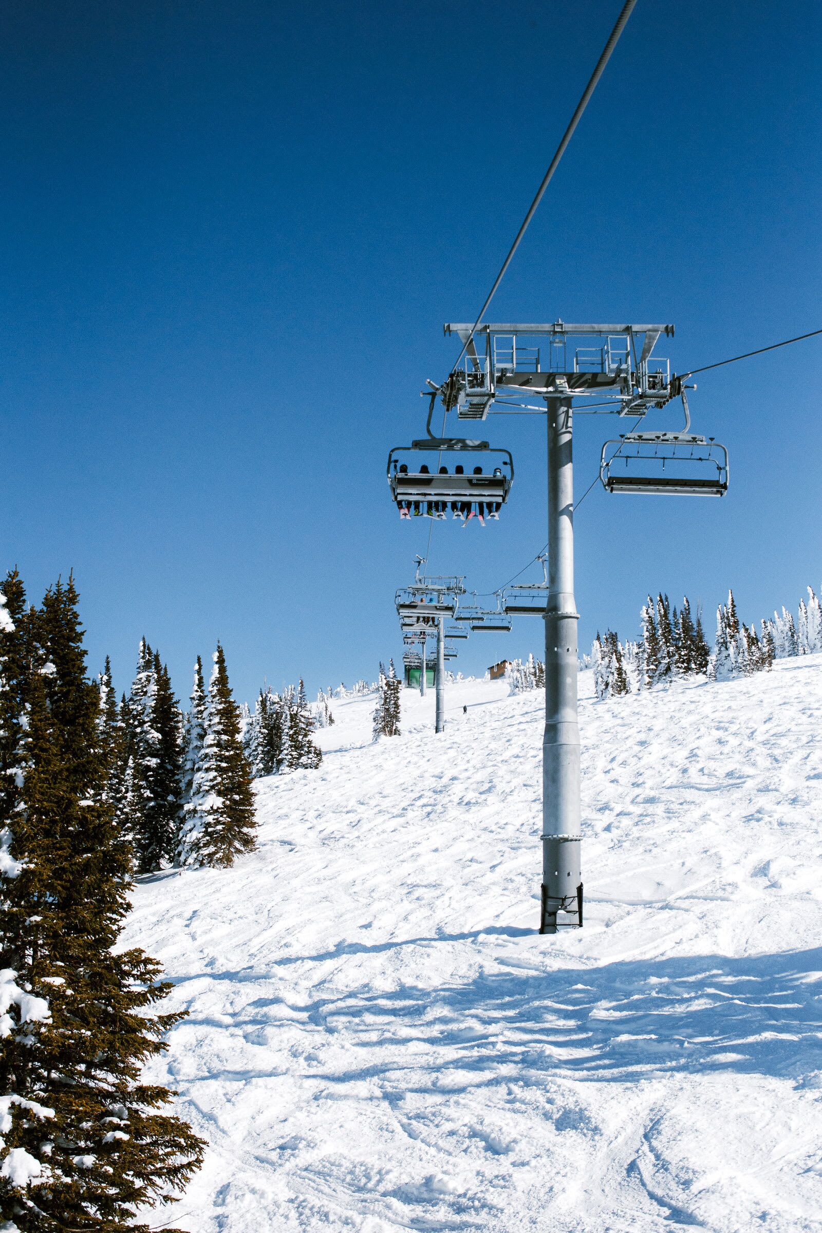 A ski lift with chairs moving up a snowy slope.