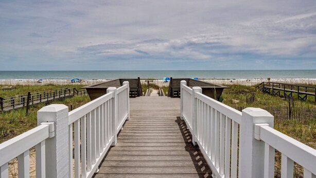 A wooden boardwalk leading to a beach with a sandy shore and a clear sky.
