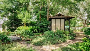 A traditional Japanese-style garden with a wooden gazebo, stone pathways, and lush greenery.