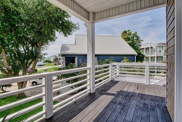 A wooden deck with white railings, a blue house in the background, and a tree in the foreground. - Relaxing Zen House! Work, relax, & play two blocks from private beach access! (Kure Beach)