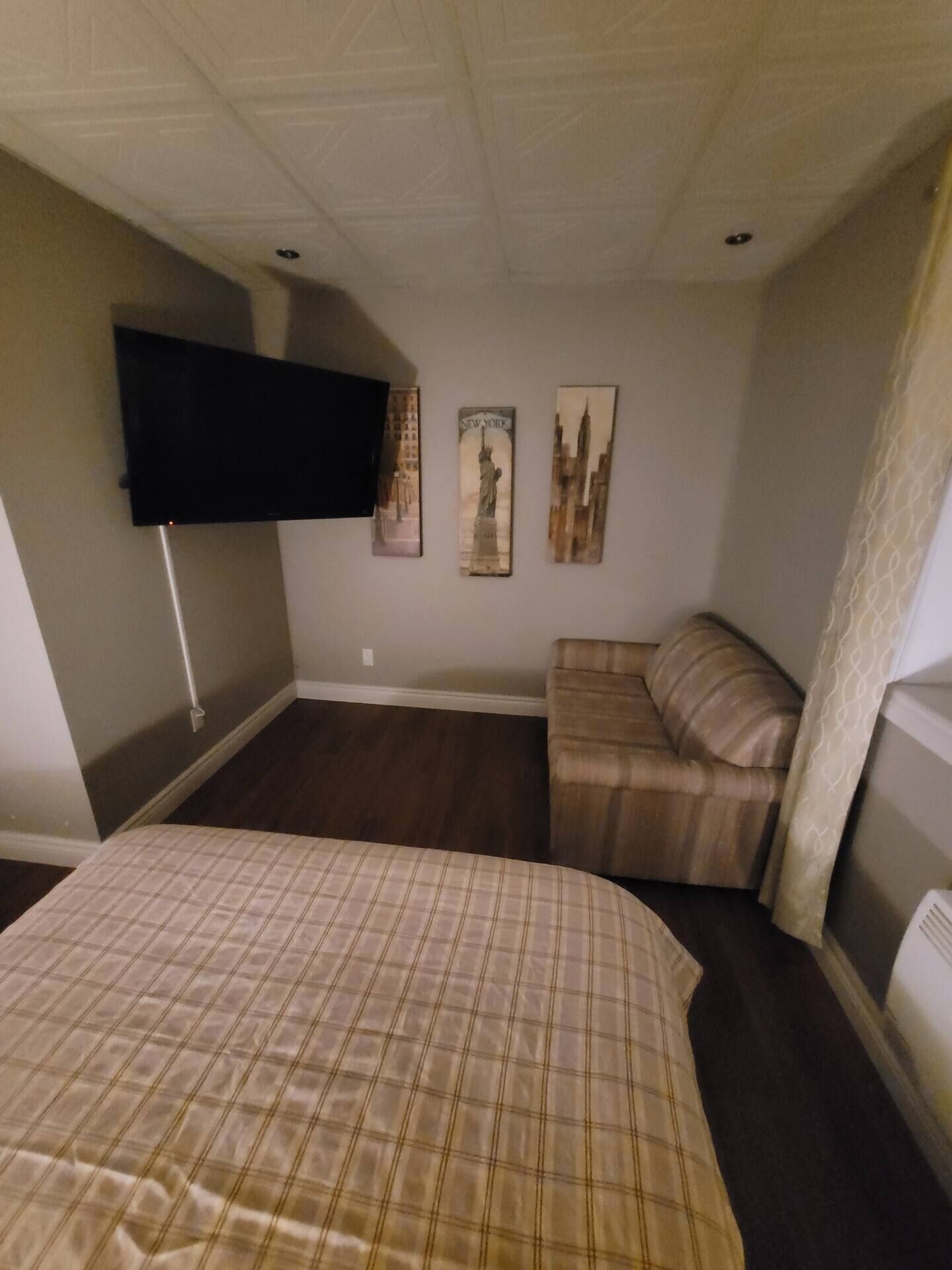 Een slaapkamer met een bed, een bank, een aan de muur bevestigde televisie en drie posters.
