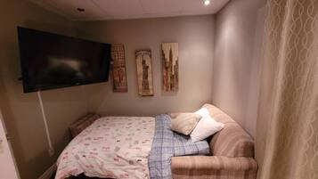 A small, cozy room with a bed, a sofa, a flat-screen TV, and wall art.
