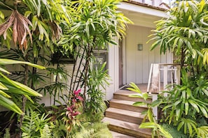 Una escalera de madera lleva a un edificio blanco, rodeado de exuberante vegetación tropical.