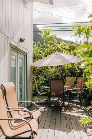 A covered outdoor seating area with chairs and a table, surrounded by lush tropical plants. - Mea Kanu Paradise, Beach Access, AC, Sleep up to 6 (Hauula)
