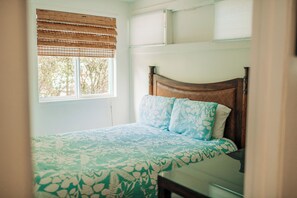 Une chambre à coucher avec un lit, une fenêtre avec des stores et une vue sur les arbres.