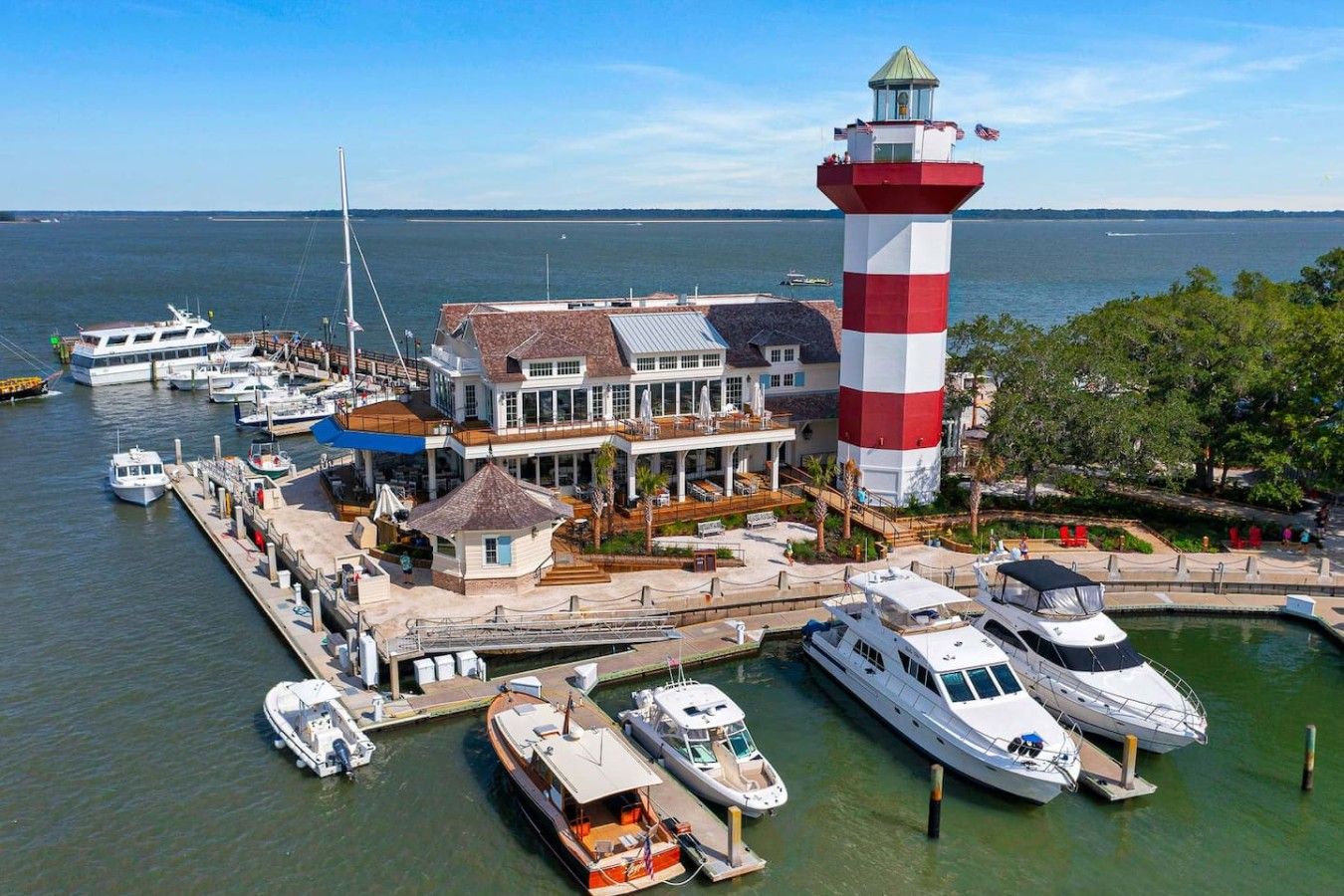 Un port de plaisance où sont amarrés de nombreux bateaux, un phare imposant et un bâtiment doté d’une terrasse.