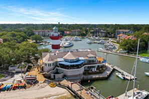 A marina with boats, a lighthouse, and a waterfront building with a deck.