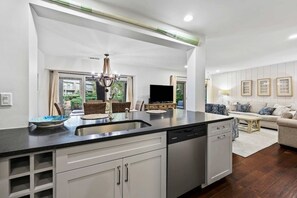 A modern kitchen with a dishwasher, a dining area with a sofa and a TV, and a living room with a couch and a coffee table.
