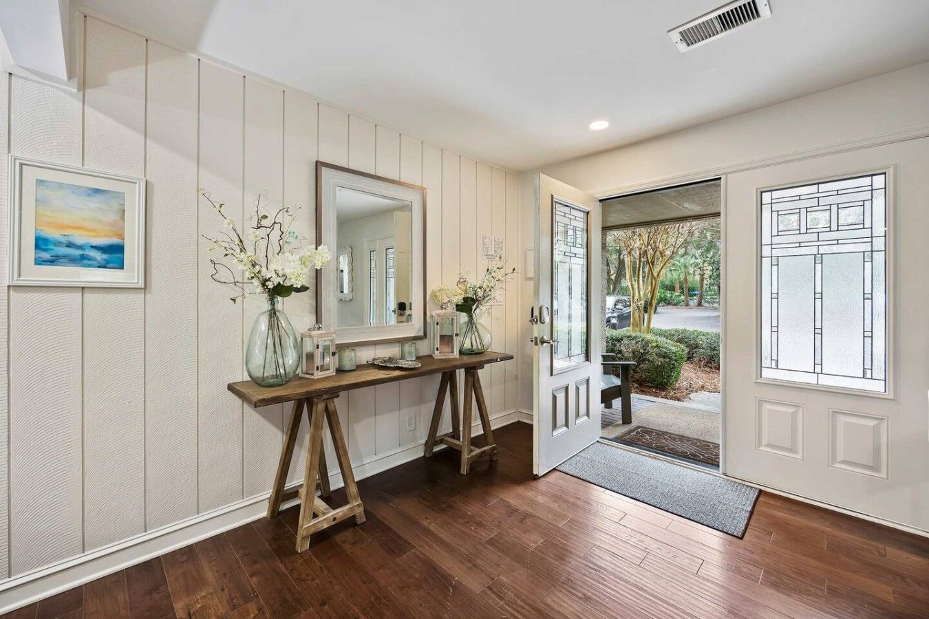 A wooden console table with vases and lanterns, a large mirror, and a door leading outside.