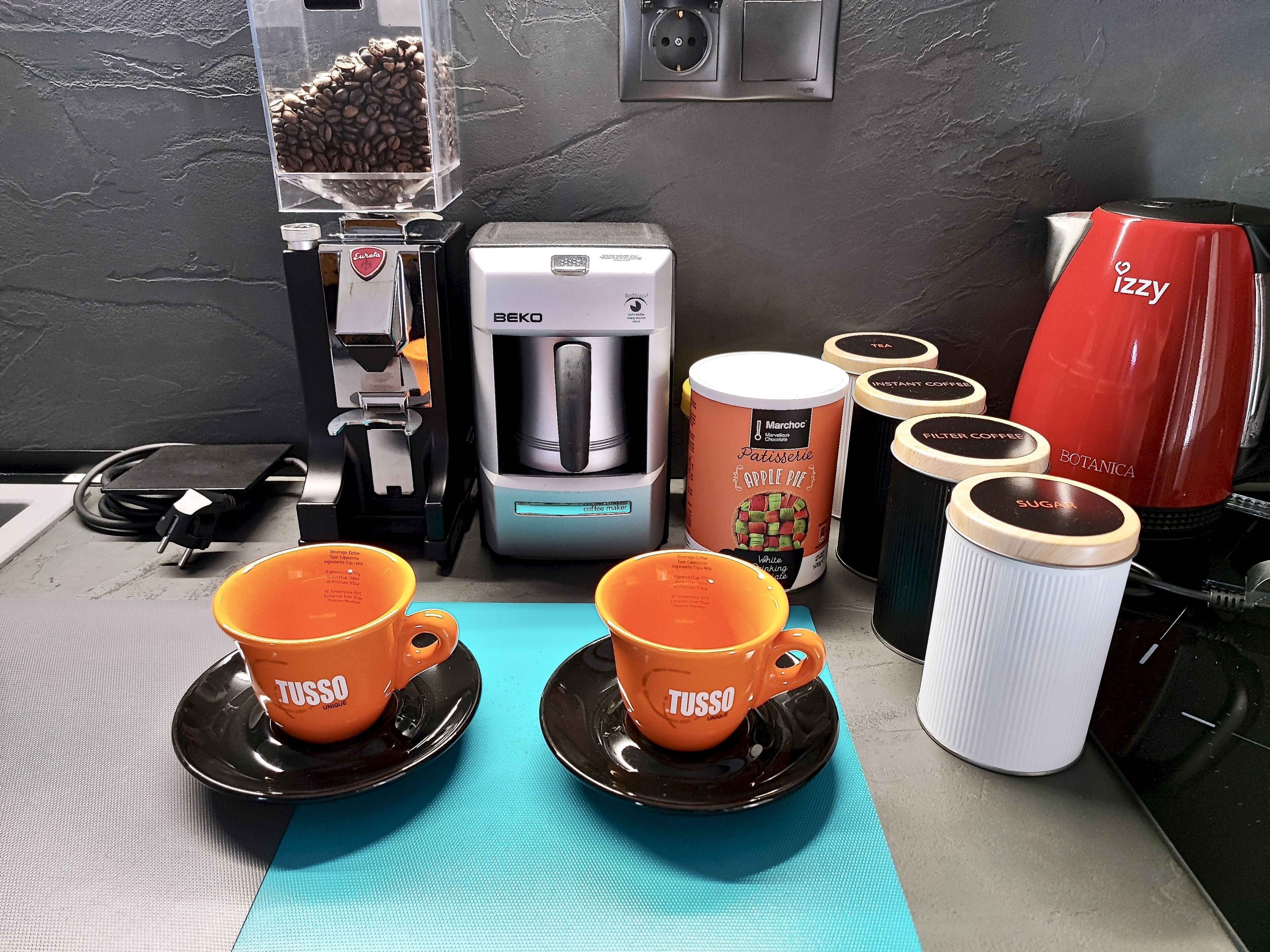 Un racó de cafè amb cafetera, molinillo i diferents càpsules de cafè.
