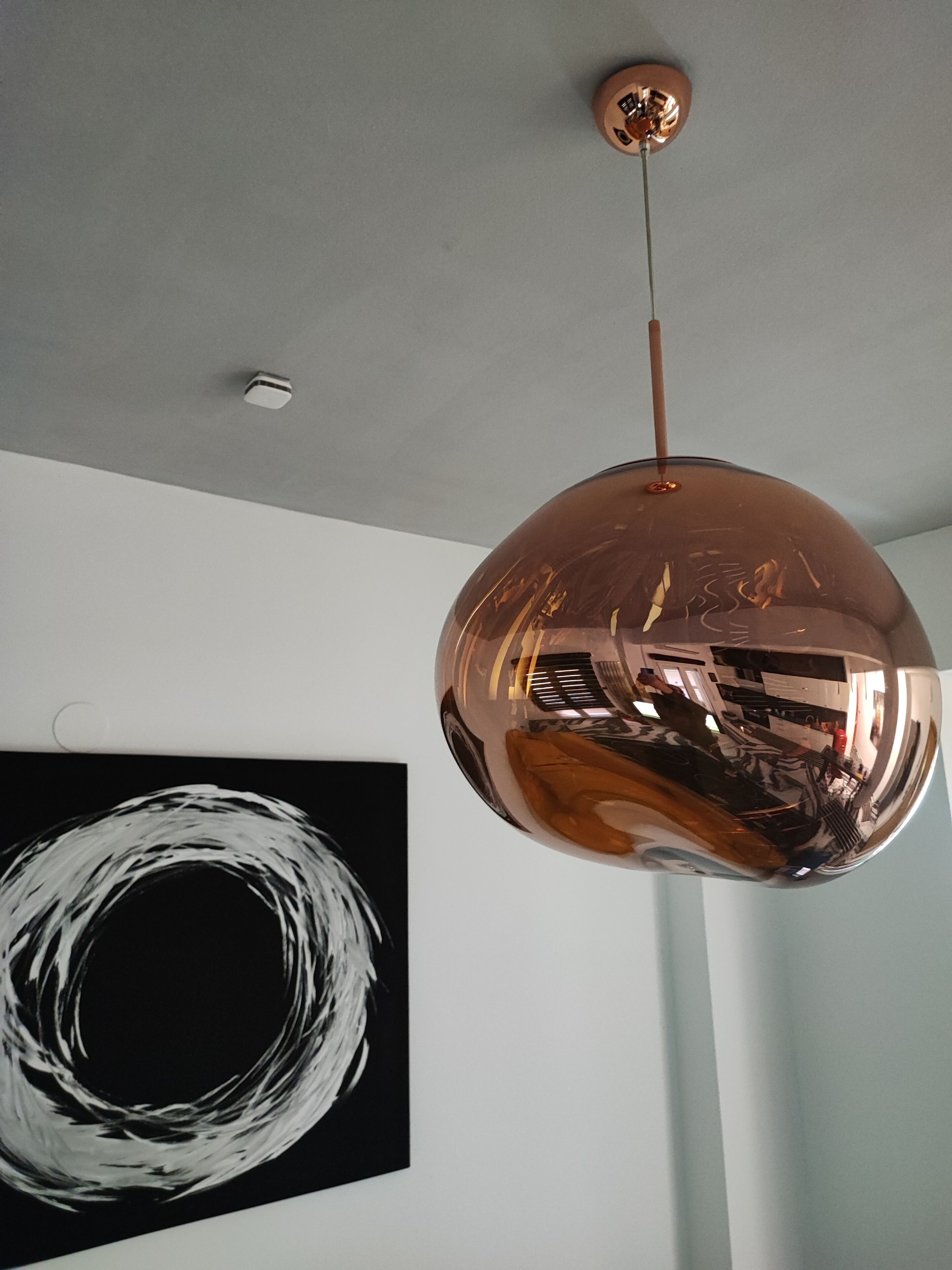 Een moderne pendellamp met een bolvormig ontwerp en koperen afwerking, hangend aan een plafond met een zichtbare rookmelder.