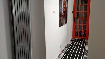Un corridoio con tappeto a righe bianche e nere, un termosifone, un quadro e una porta rossa con la scritta 'TELEPHONE'.