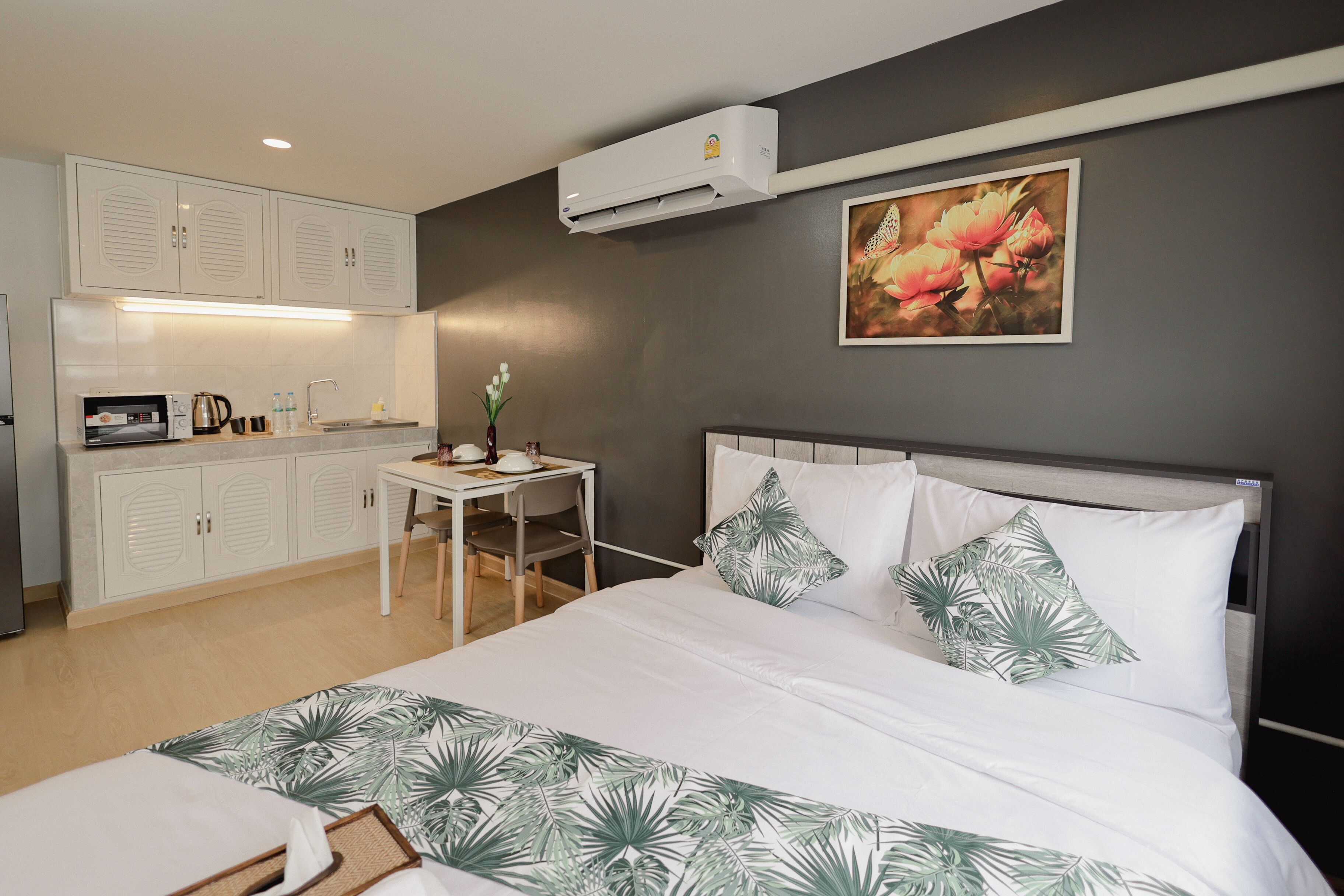 A hotel room with a bed, a desk with a chair, a microwave, and a small table with a vase of flowers.
