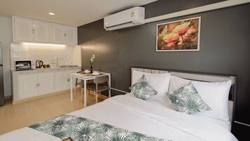 A hotel room with a bed, a desk with a chair, a microwave, and a small table with a vase of flowers.