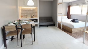 A compact hotel room with a dining area, a sofa, a bed, and a kitchenette. - DHIresidence at Impact Muangthong (Pak Kret)
