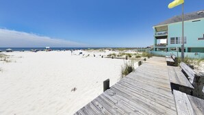 A beach with a wooden boardwalk leading to a building with a yellow flag. - Sanibel 1604 (Gulf Shores)