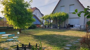 A residential backyard with a wooden deck, outdoor furniture, and a stone pathway. - Gîte Alsace Maison Avec Jardin Proche Strasbourg (Mutzig)