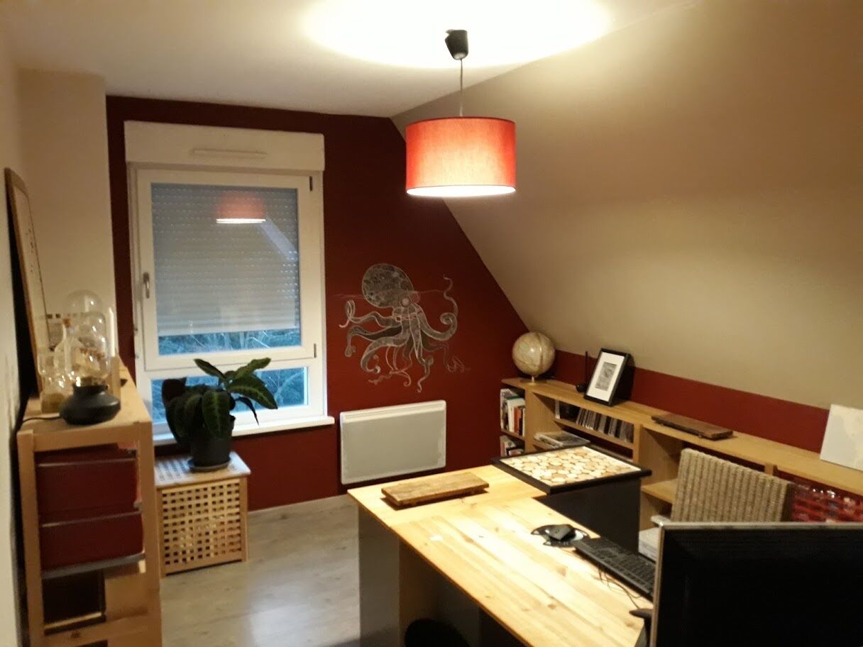 A cozy attic bedroom with a sloped ceiling, a large window, a wooden desk, a globe, and a wall mural.