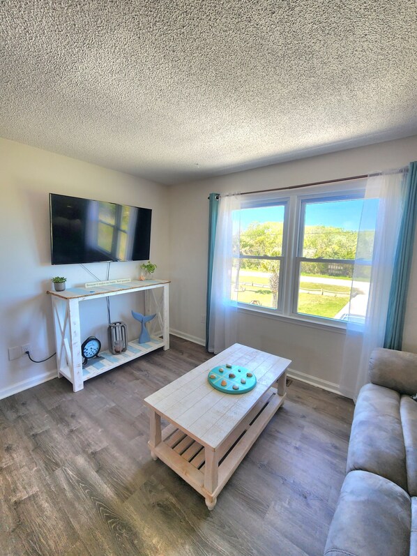 A living room with a television, a small table with a decorative item, a sofa, and a window with curtains.