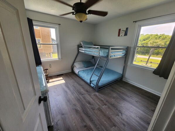 A room with a bunk bed, a ceiling fan, and a window with a view of greenery.