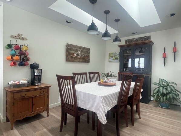 A dining area with a table set for four, surrounded by wooden chairs, a coffee maker, and a coffee mug rack on the wall. - Home Away from Home with Mountain Views over Oxford Hills (Otisfield)