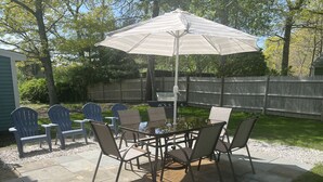 Un patio al aire libre con mesa y sillas, una parrilla y un gran parasol.