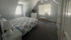 Un dormitorio con cama, escritorio, silla, ventilador de techo y ventana con persianas.
