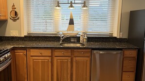 Una cocina con armarios de madera, un lavamanos de acero inoxidable y un lavavajillas integrado.